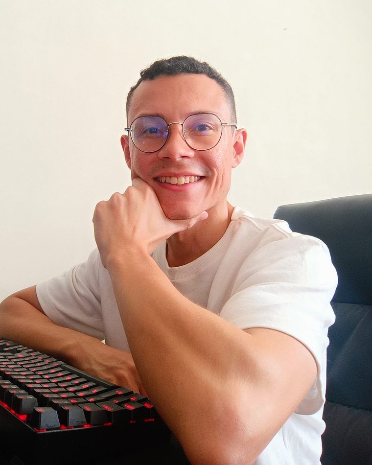 Patrick Ribeiro sorrindo na mesa de trabalho, ao lado do teclado